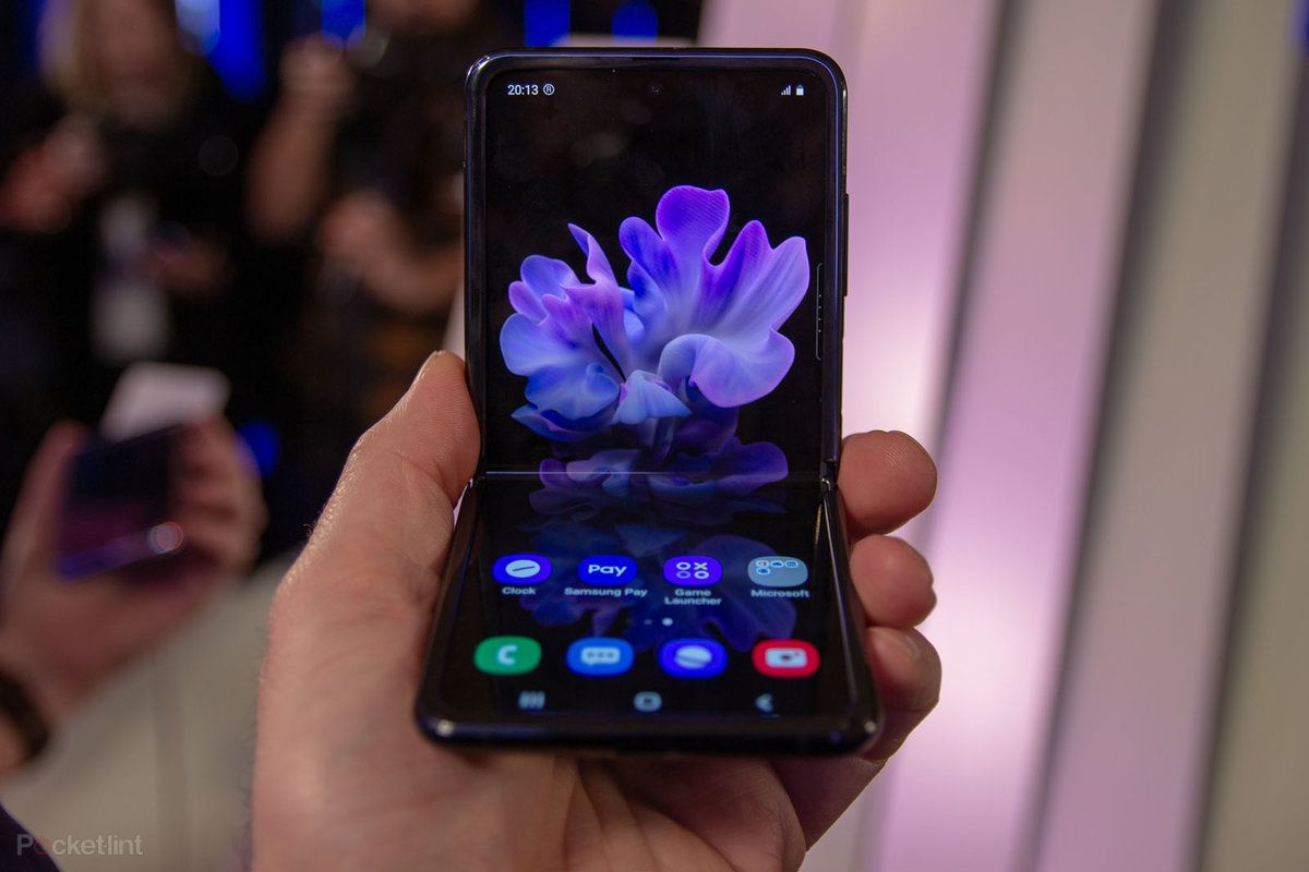 Terdapat tangan yang memegang smartphone Galaxy Z Flip yang hampir terlipat dengan layar yang menunjukkan gambar bunga berwarna biru